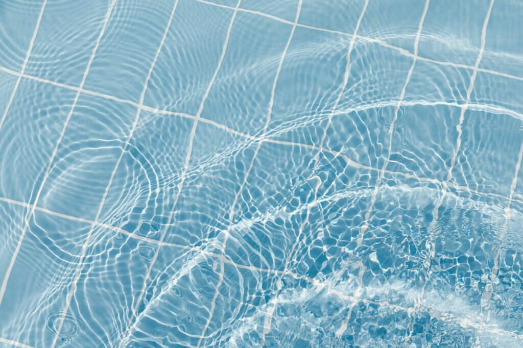 Clear water surface with ripple wave splashes and drops in swimming pool.